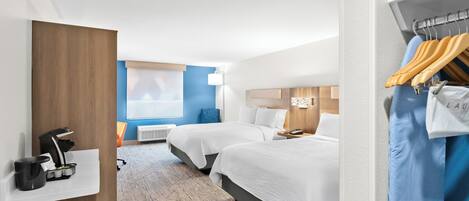 A hotel room with two beds, a coffee machine, a wardrobe, and a window with blinds.