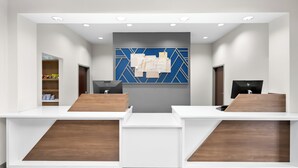 A reception area with a modern design, featuring a central blue and gold geometric wall art, two reception desks with wooden accents, and a digital display monitor. - Holiday Inn Express & Suites Morrilton by IHG (Morrilton)