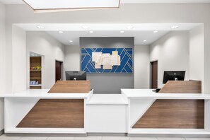 A reception area with a modern design, featuring a central blue and gold geometric wall art, two reception desks with wooden accents, and a digital display monitor. - Holiday Inn Express & Suites Morrilton by IHG (Morrilton)