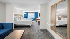 Une chambre d’hôtel avec un grand lit, un lit plus petit, un bureau, une chaise, un canapé bleu et un grand miroir.
