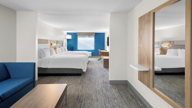 A hotel room with a large bed, a smaller bed, a desk, a chair, a blue sofa, and a large mirror. - Holiday Inn Express & Suites Morrilton by IHG (Morrilton)