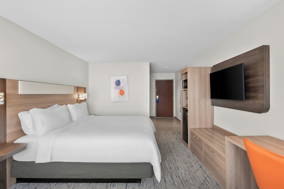 A modern hotel room with a large bed, a flat-screen TV mounted on the wall, and a wooden nightstand.