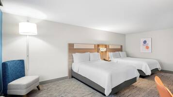 A hotel room with two beds, a desk, a chair, a lamp, and a wall art piece.