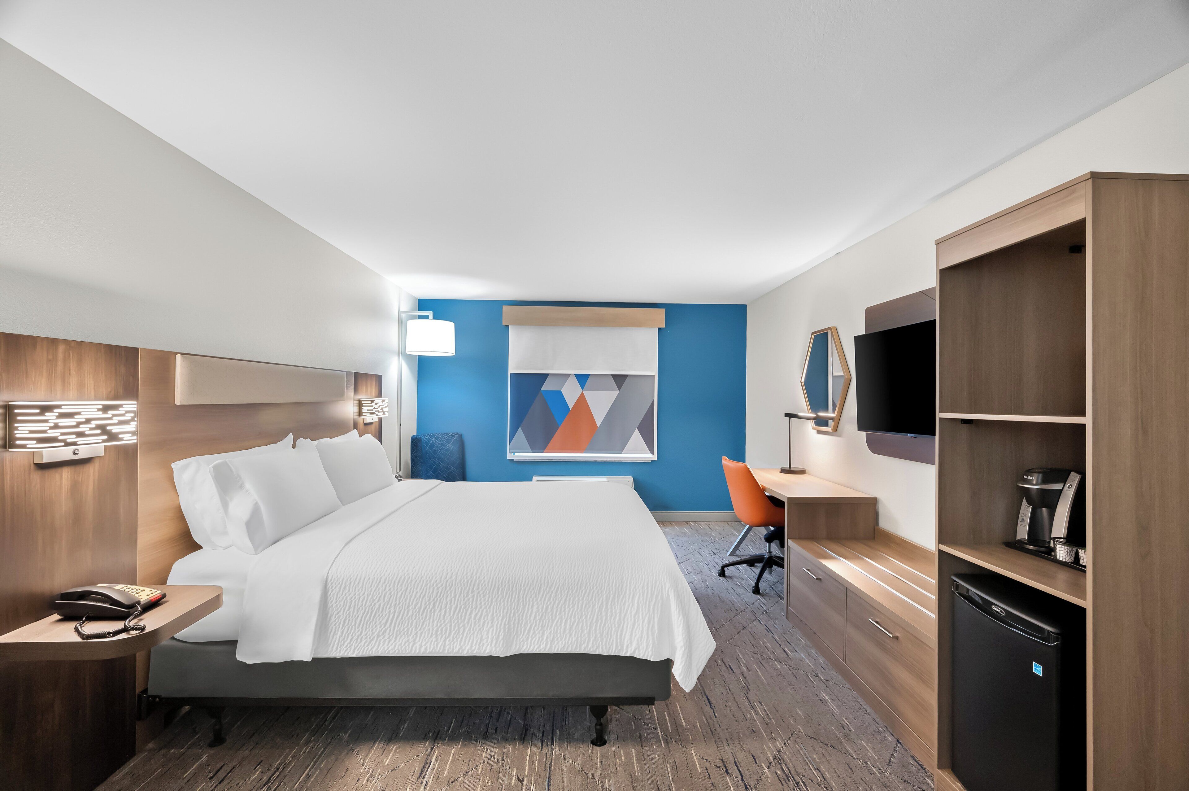 Habitación de hotel con cama, escritorio, silla, televisor y cafetera.