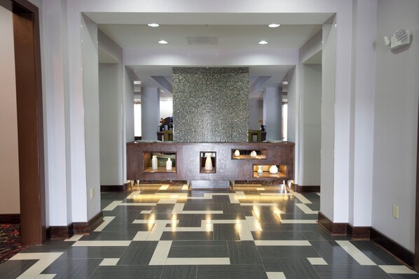Zona de recepción de hotel con mostrador de registro, una pared decorativa con mosaicos y piso estampado.
