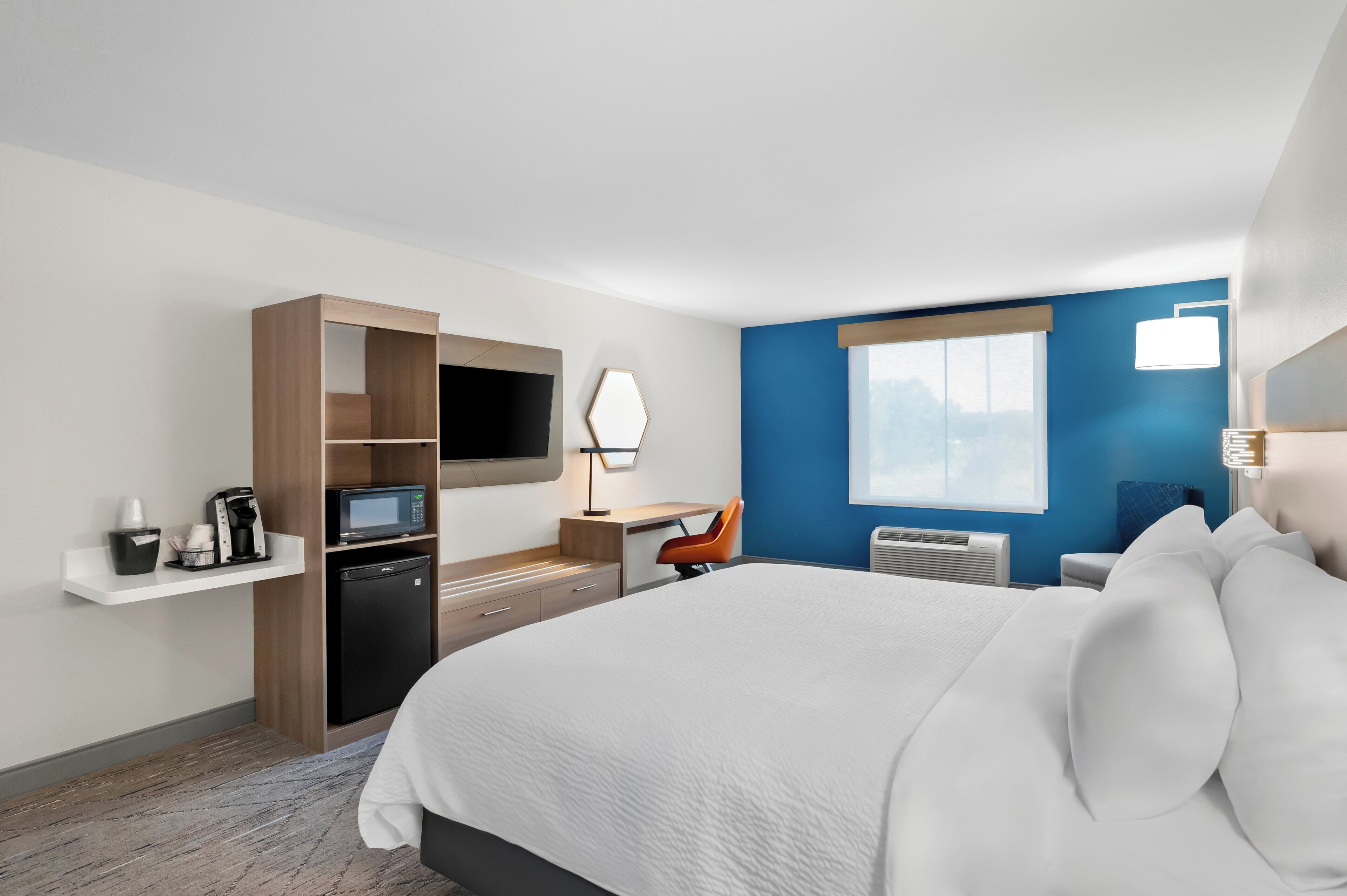 A hotel room with a bed, a desk, a chair, a TV, a microwave, a coffee maker, and a window.