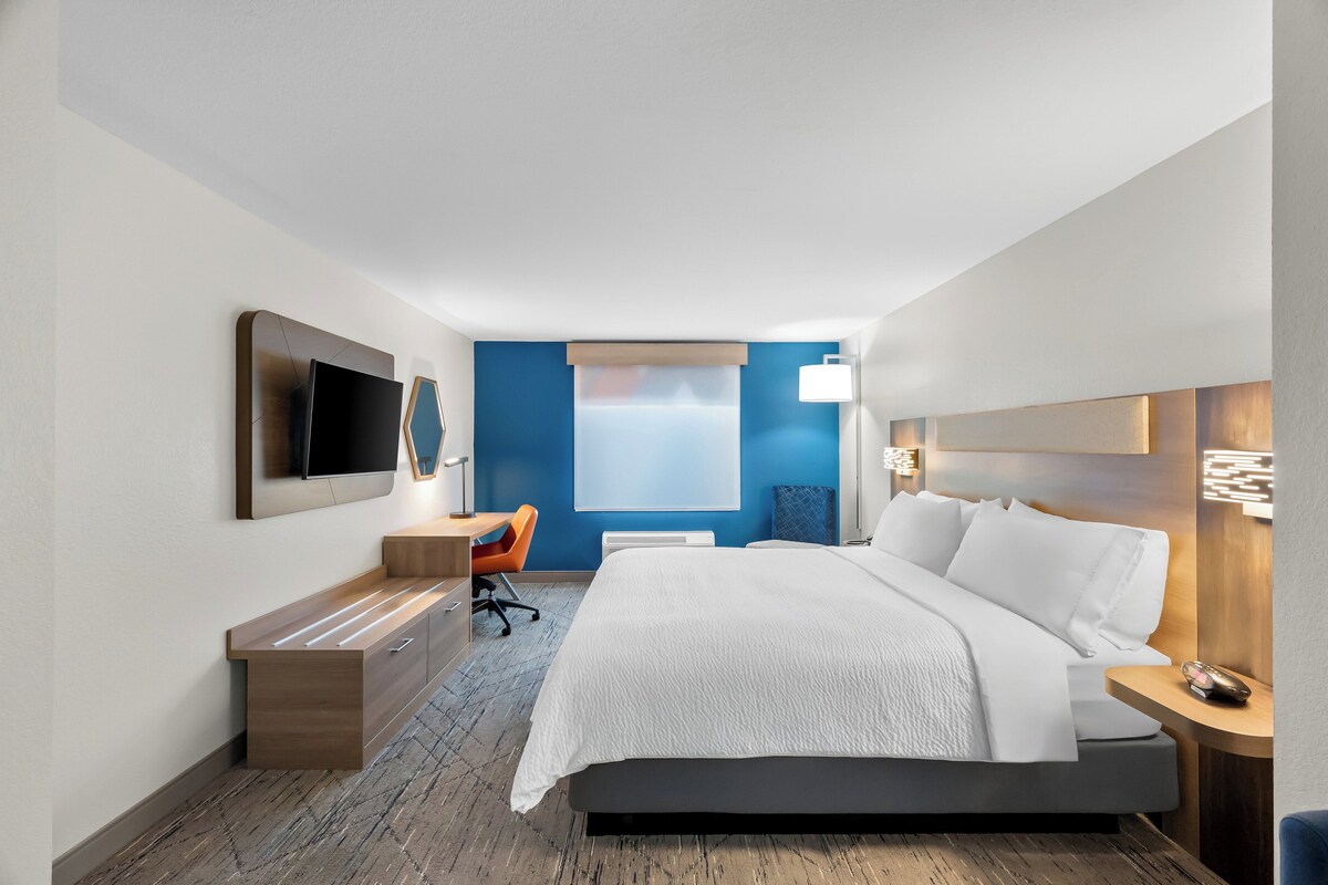 A modern hotel room with a large bed, a desk, a chair, a flat-screen TV, and a window with a view.