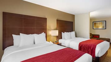 A hotel room with two beds, a nightstand, a lamp, a chair, and a painting on the wall.