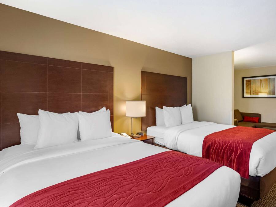 A hotel room with two beds, a nightstand, a lamp, a chair, and a painting on the wall.