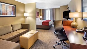 A hotel room with a sofa, a desk with a lamp, a bed with a red blanket, and a television. - Comfort Inn & Suites Tooele - Salt Lake City (Tooele)