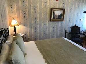 Un dormitorio con cama, lámpara, sillón y un cuadro en la pared.