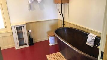 Un baño con bañera, un banco de madera, un inodoro, un perchero y un armario pequeño.