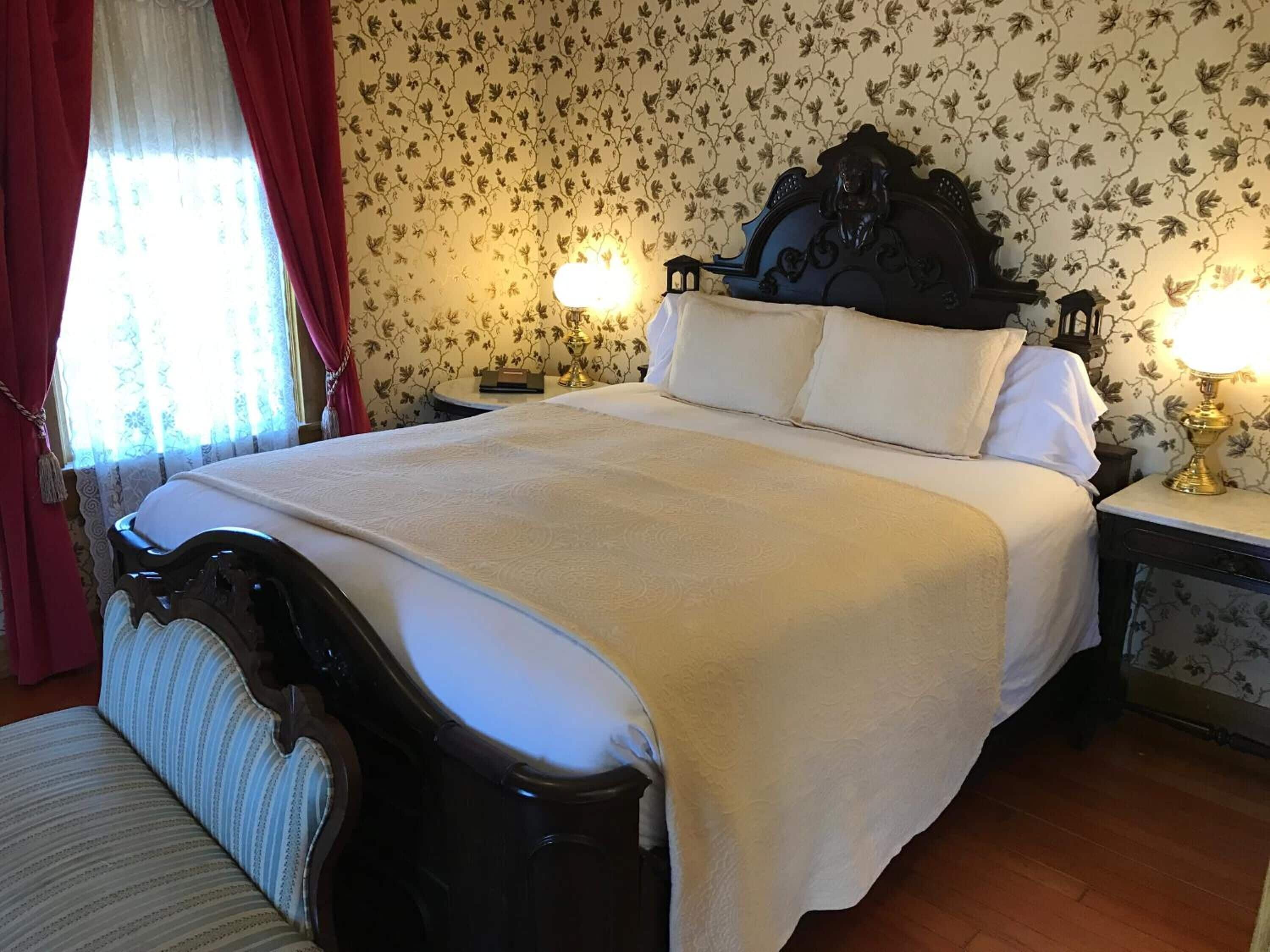A neatly made bed with a dark headboard, white linens, and two bedside lamps.