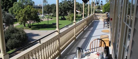 A balcony with a table set for breakfast, overlooking a park with trees and a statue.
