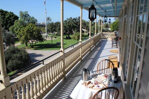 A balcony with a table set for breakfast, overlooking a park with trees and a statue. - Cosmopolitan Hotel & Restaurant (San Diego)