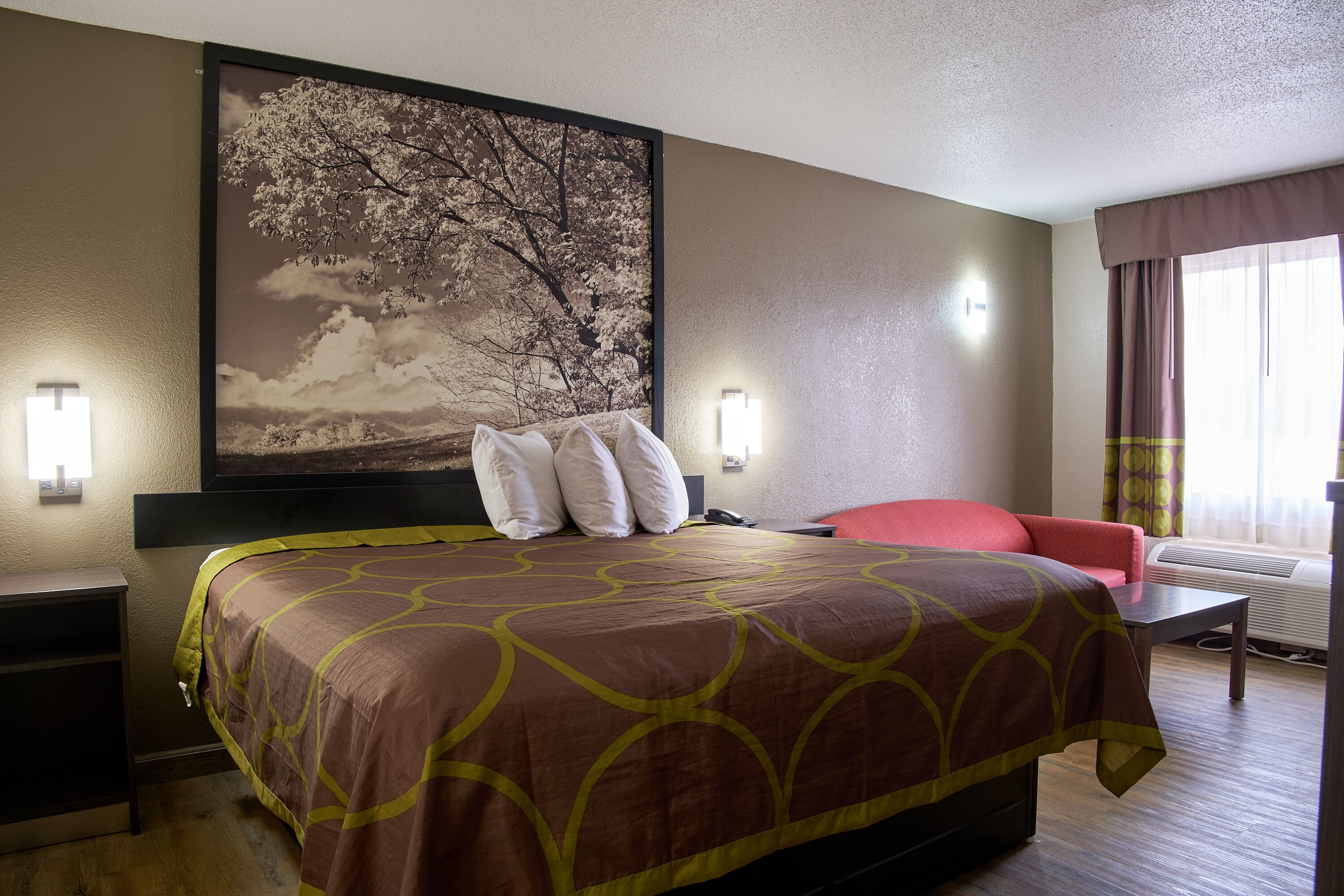 Une chambre d’hôtel avec un grand lit, un fauteuil rouge, un bureau et un téléviseur fixé au mur.