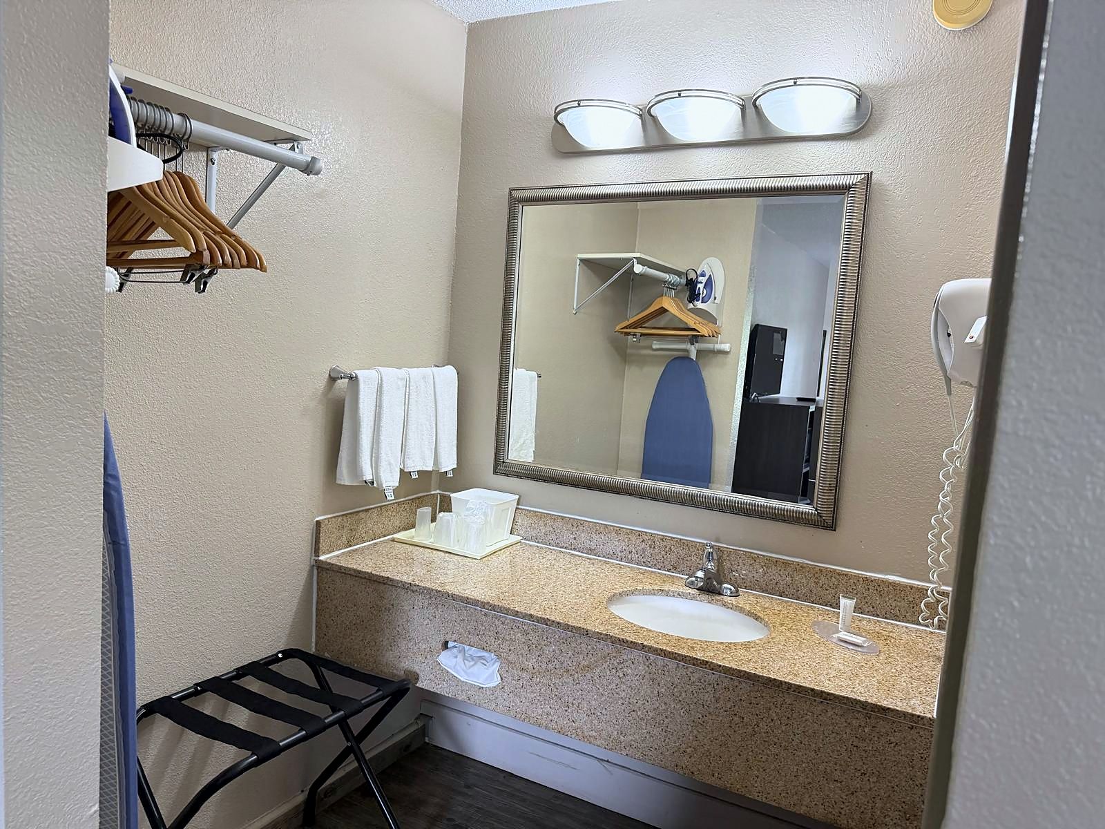 Une salle de bain équipée d’un lavabo, d’un miroir, d’un porte-serviettes et d’un petit étendoir noir.