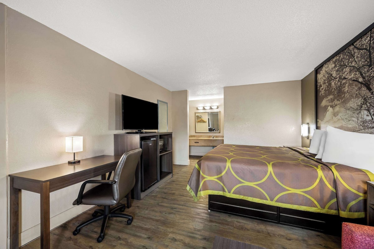 A hotel room with a bed, desk, chair, TV, and a bathroom with a mirror.