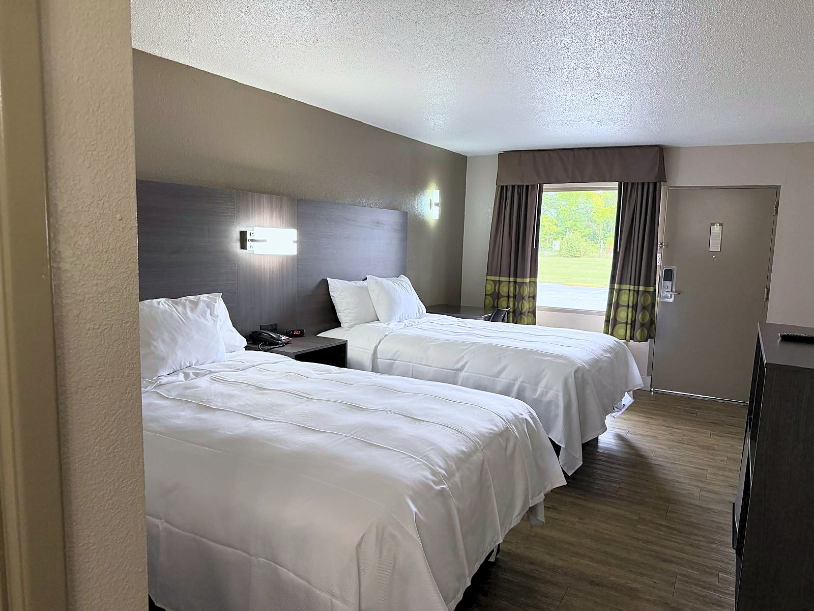 A hotel room with two beds, a nightstand, a desk, a chair, a window with curtains, and a door.