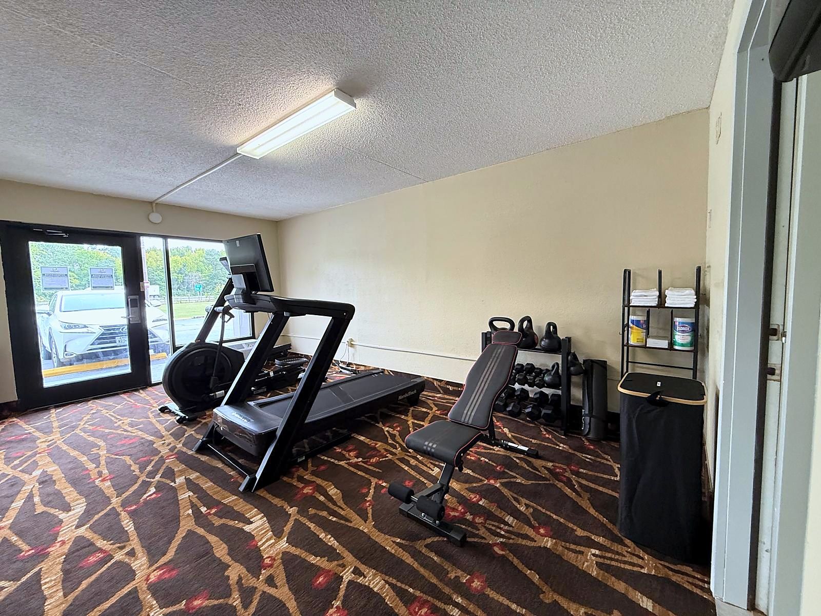 Ein Hotelzimmer mit Laufband, einer Sitzbank, Kettlebells und einem Fernseher.