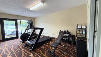 Ein Hotelzimmer mit Laufband, einer Sitzbank, Kettlebells und einem Fernseher.