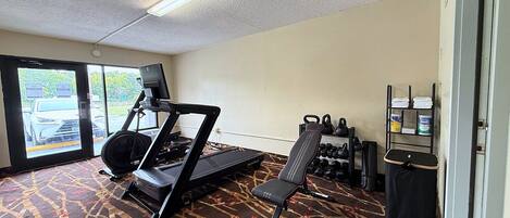 A hotel room with a treadmill, a bench, kettlebells, and a TV.
