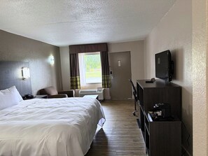Una habitación de hotel con cama, escritorio, silla, televisión y ventana con cortinas.