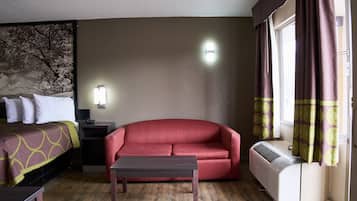 A hotel room with a bed, a red sofa, a small table, a heater, and a window with curtains.