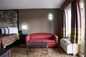 A hotel room with a bed, a red sofa, a small table, a heater, and a window with curtains. - Quality Inn (Garysburg)