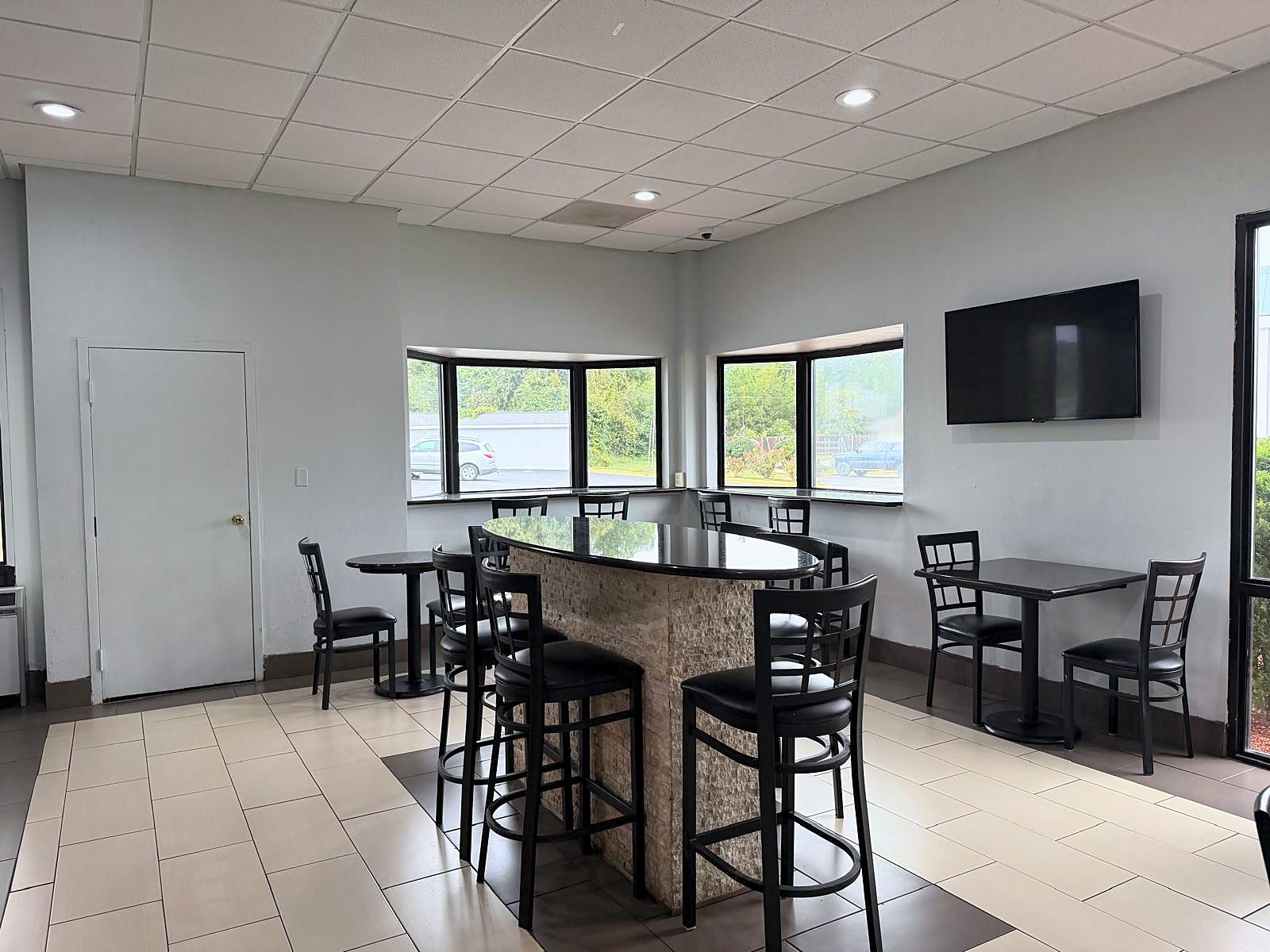 A spacious room with a central island table surrounded by chairs, large windows with a view of the outdoors, and a flat-screen TV mounted on the wall.