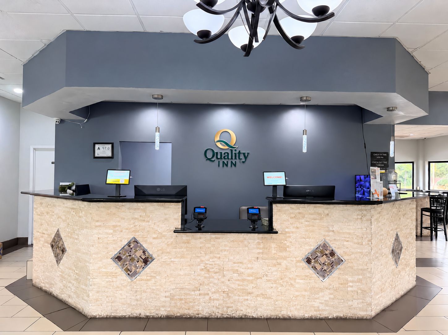 A hotel reception desk with a modern design, a chandelier, and a digital screen displaying the hotel name.