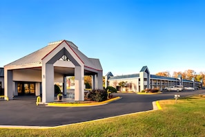 Un hotel con un techo triangular característico, un acceso cubierto y un estacionamiento.