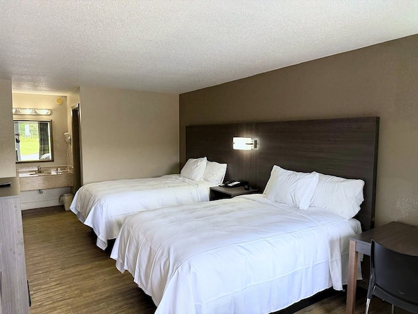 Habitación de hotel con dos camas, un escritorio, un espejo y una mesita de noche con lámpara.