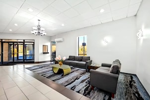 A modern hotel lobby with a grey sofa, a coffee table with a vase of flowers, a chandelier, and a large window with a view of trees.