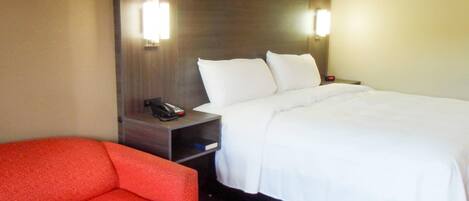 A hotel room with a bed, a nightstand, a telephone, and a red chair.