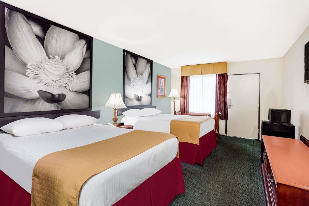 A hotel room with two beds, a desk, a television, and artwork on the walls.