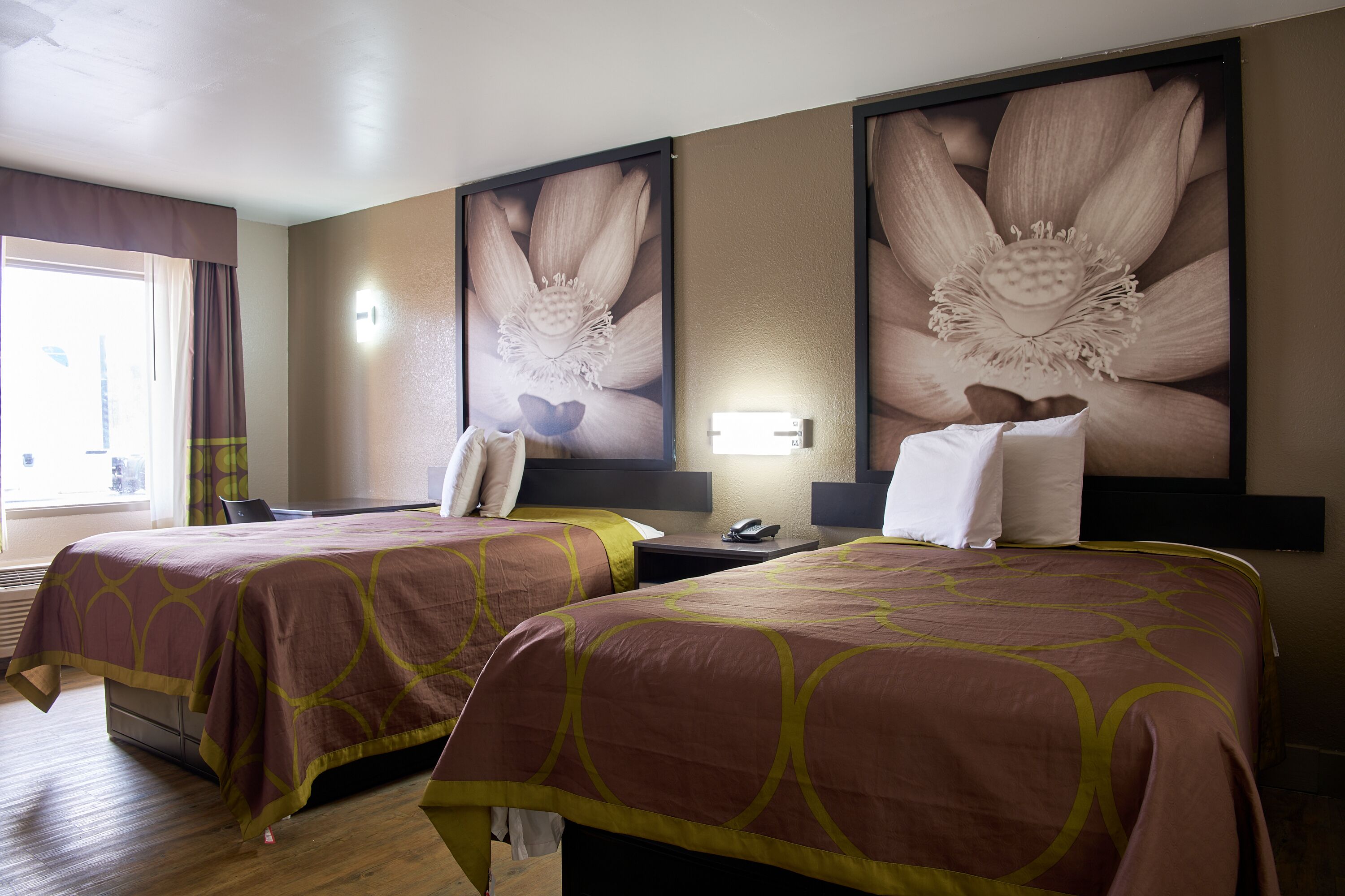 Habitación de hotel con dos camas, un escritorio, una silla, un teléfono y una obra de arte floral grande en la pared.