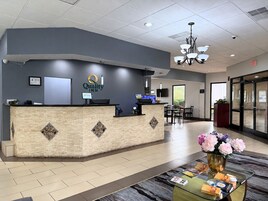 A reception area with a reception desk, a 'Quality Inn' sign, a television, and a seating area with a table and chairs.