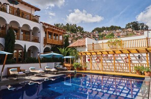 Zona de piscina con sillones de descanso, sombrillas y vistas a un pueblo en la ladera.