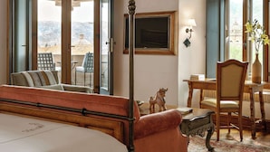 Una cama con dosel, un escritorio, una silla y un televisor montado en la pared en una habitación con vista a las montañas.