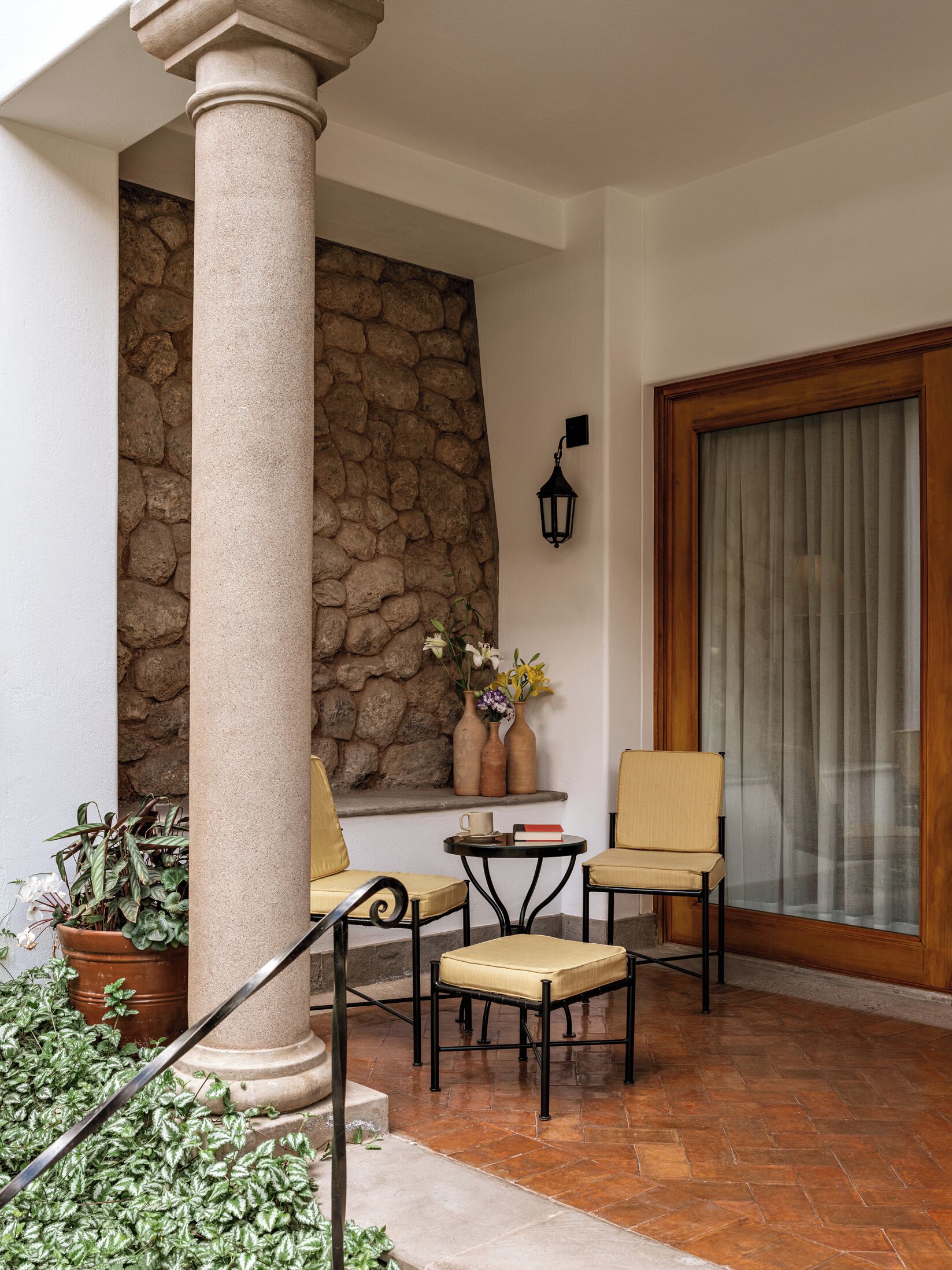 Un espace patio comprenant deux chaises, une table, un mur en pierre, une plante en pot et une porte en bois.