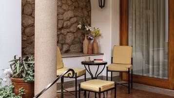 Un espace patio comprenant deux chaises, une table, un mur en pierre, une plante en pot et une porte en bois.