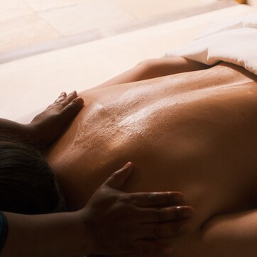 A person lying on a bed with a hand on their back, a white pillow, and a wooden door in the background.