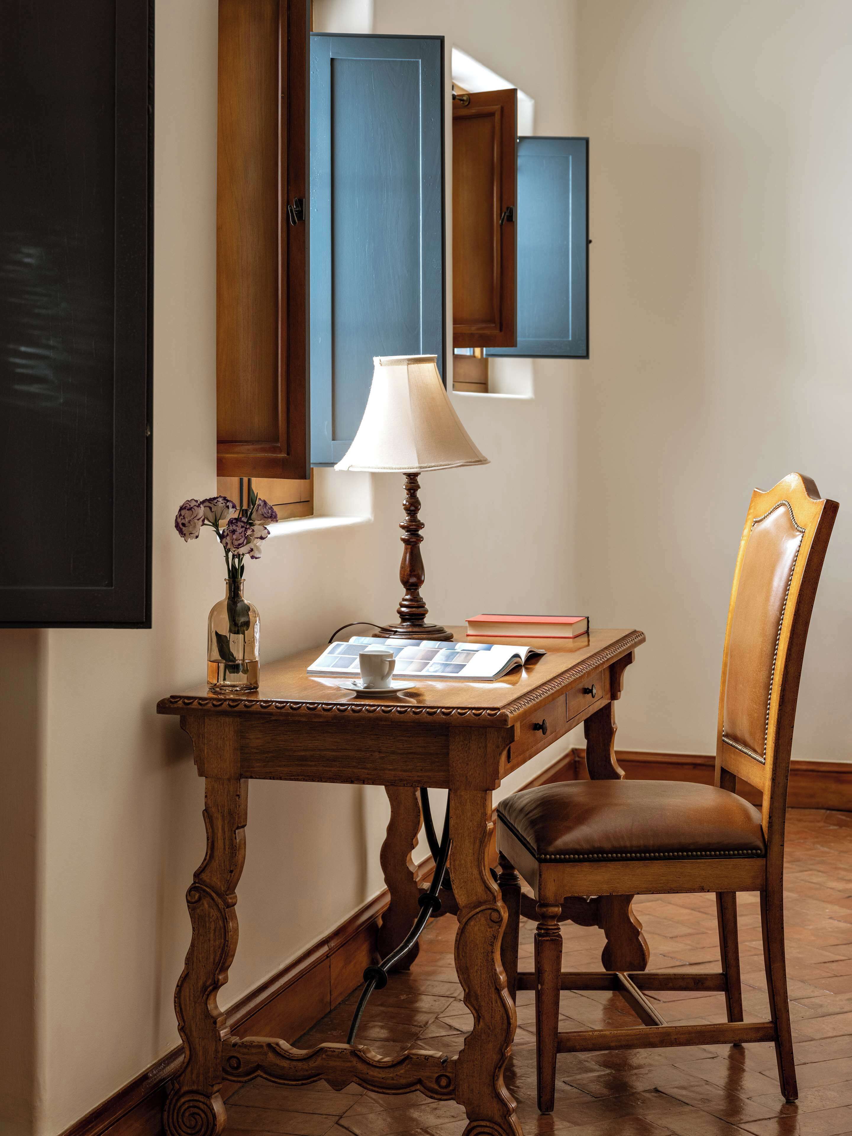 Een houten bureau met een lamp, een stoel, een boek en een fles erop.