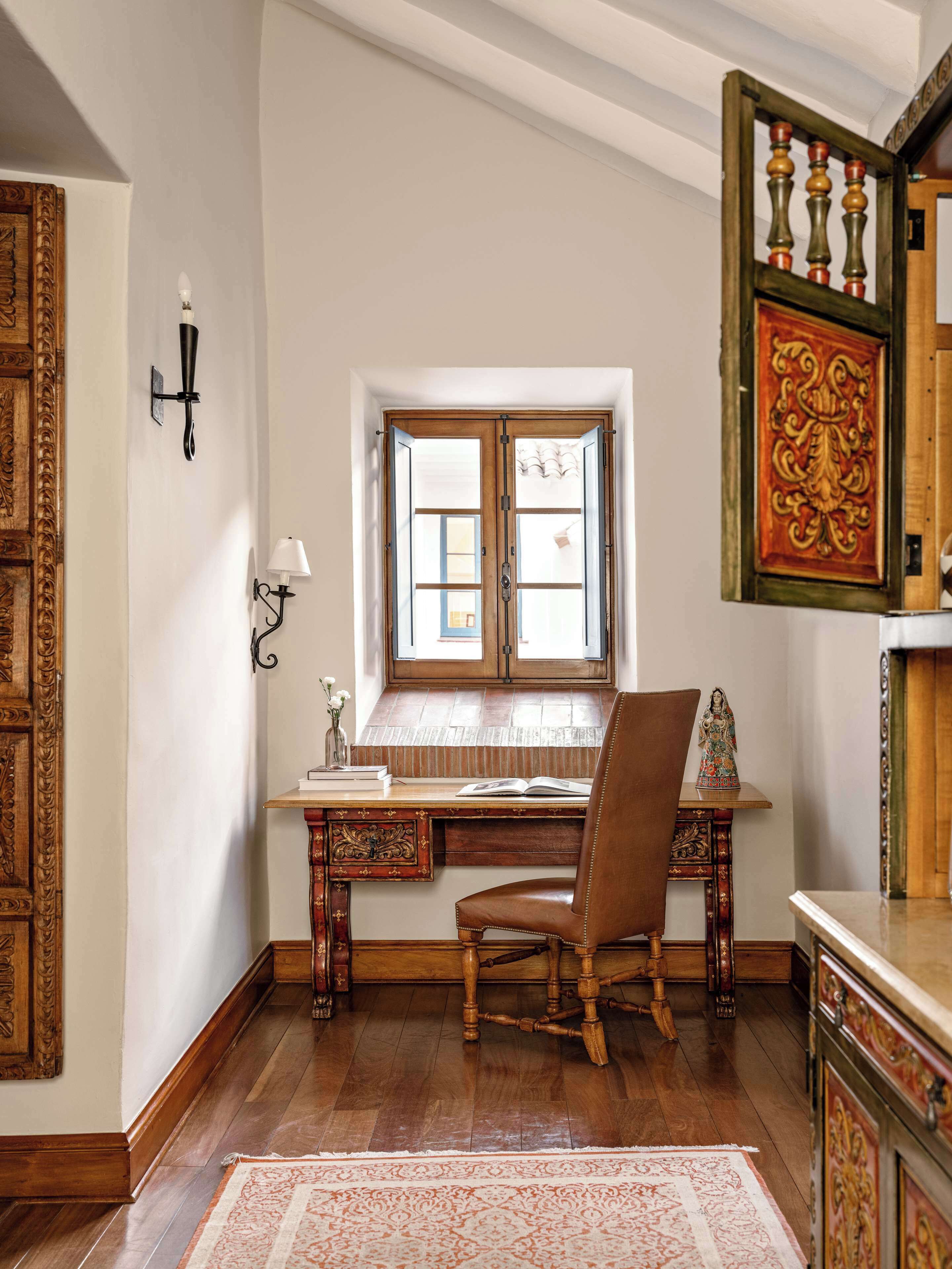 Habitació tradicional amb escriptori de fusta, una cadira, finestra amb vistes i un element decoratiu a la paret.