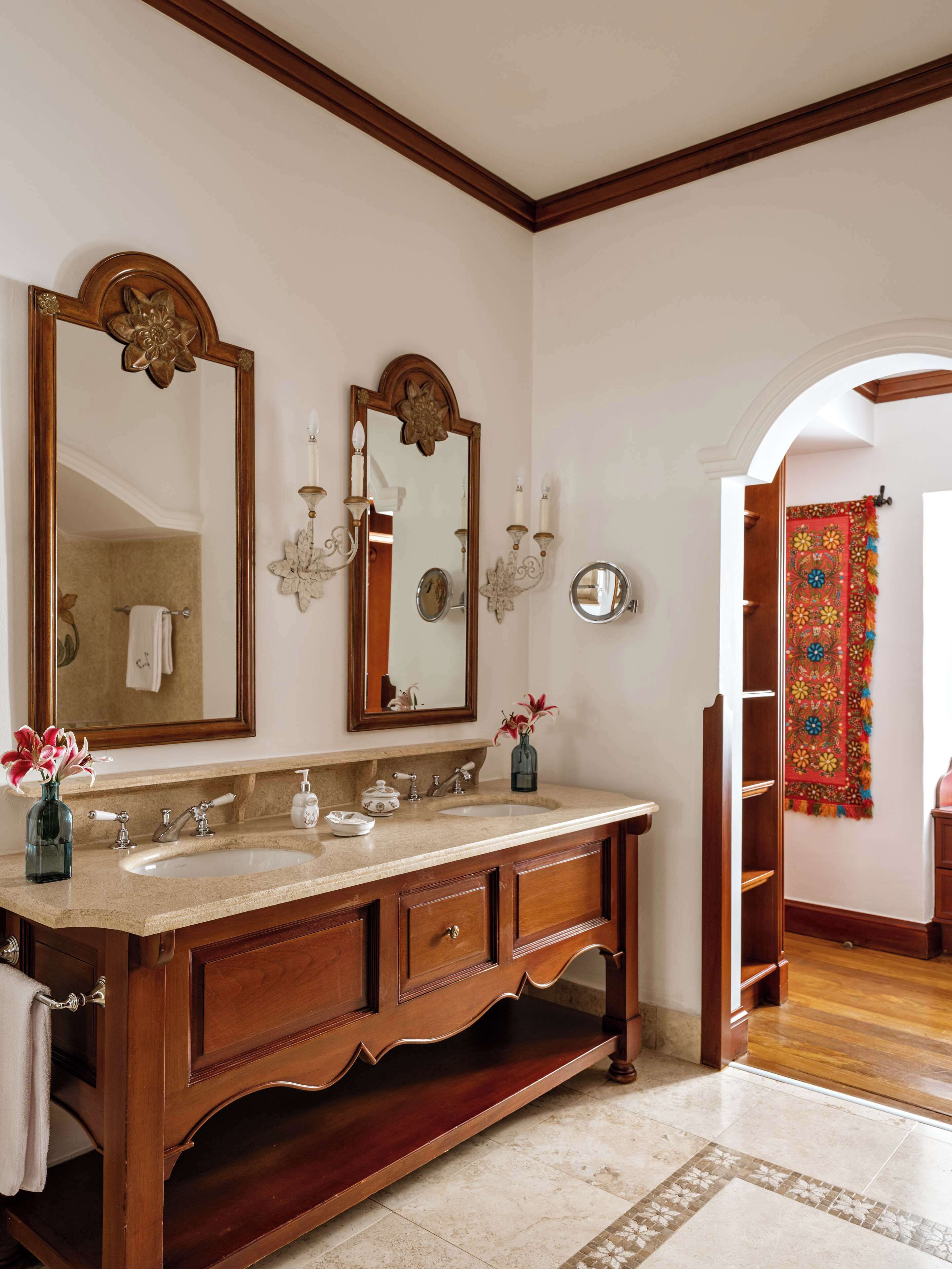 A bathroom with a wooden vanity, two sinks, a large mirror, wall sconces, and a decorative tapestry.