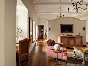 A spacious living room with a wooden floor, a sofa, a coffee table, a TV, and a chandelier.