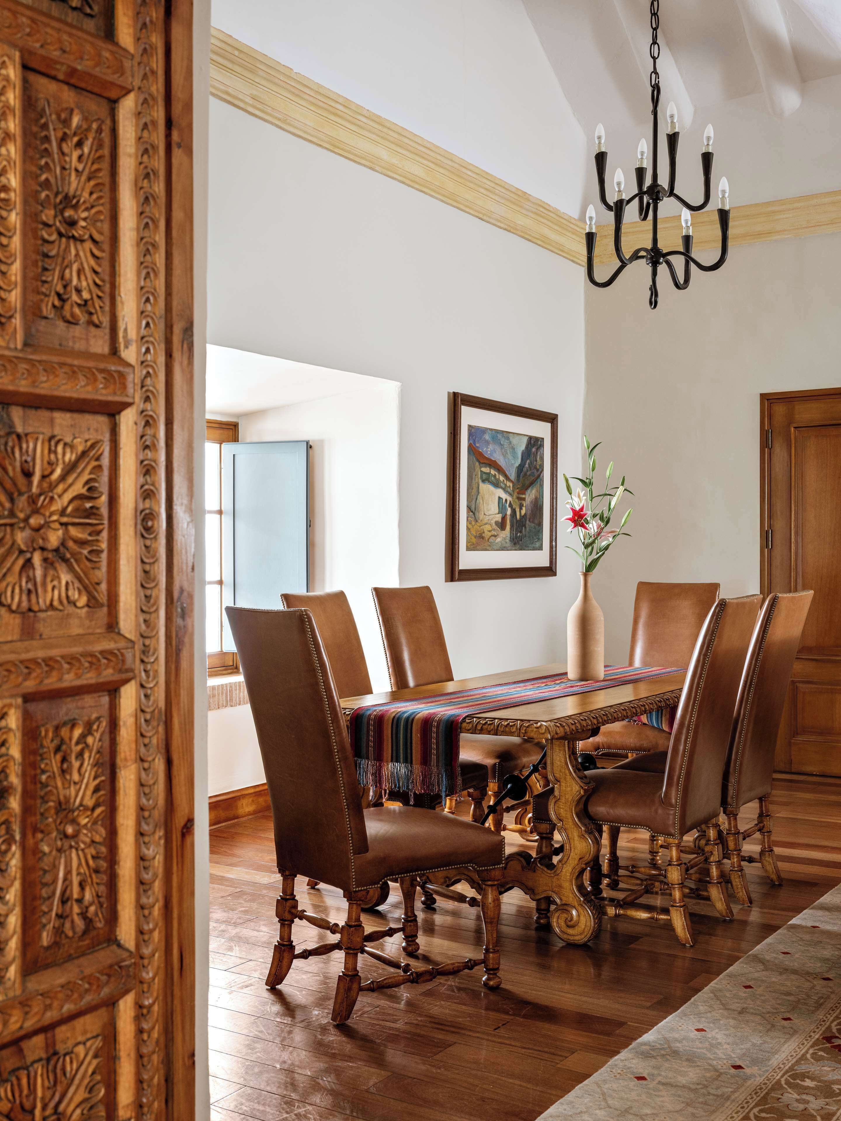 A dining room with a wooden table, leather chairs, a chandelier, and a framed painting on the wall.