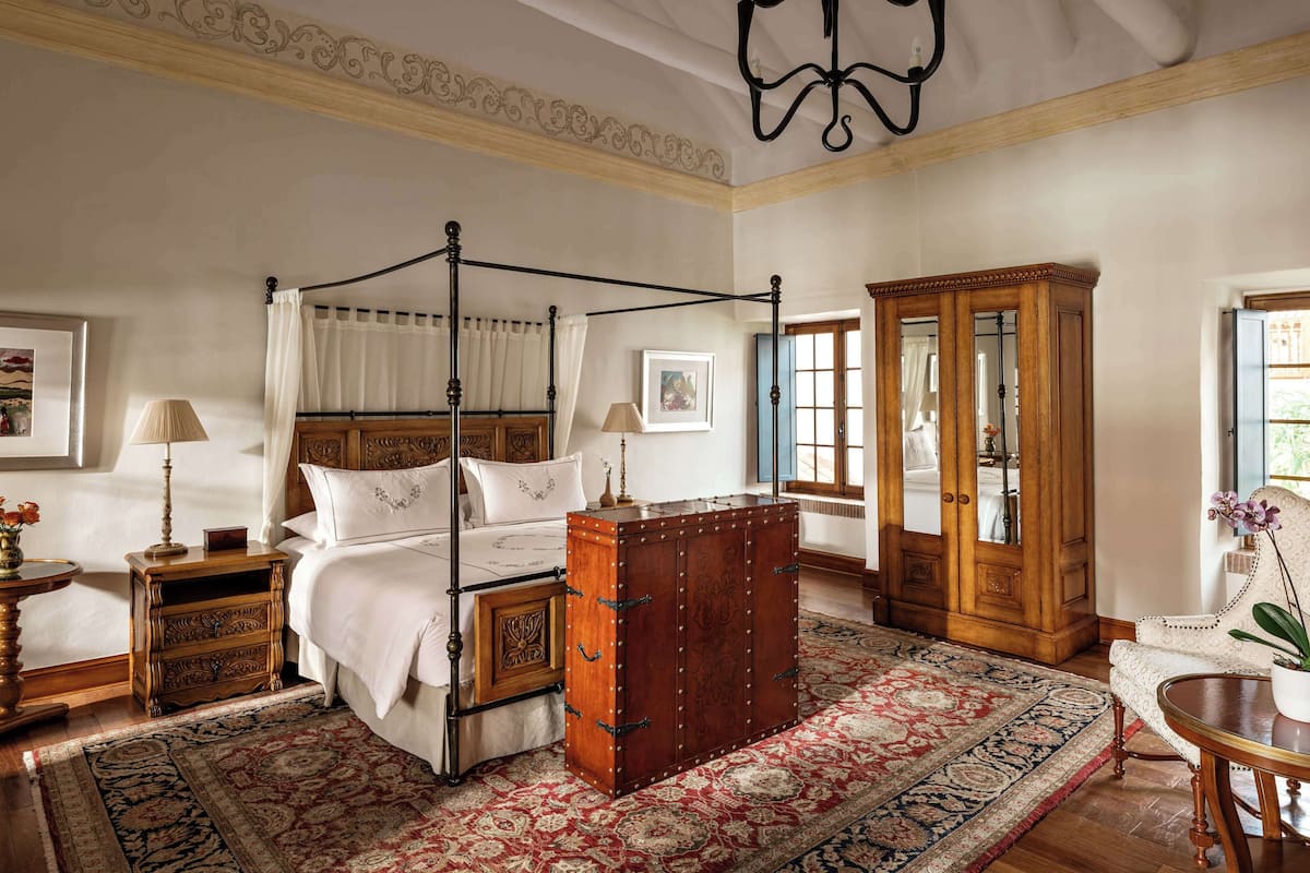 A four-poster bed with a wooden headboard, a large wooden cabinet, and a red patterned rug.