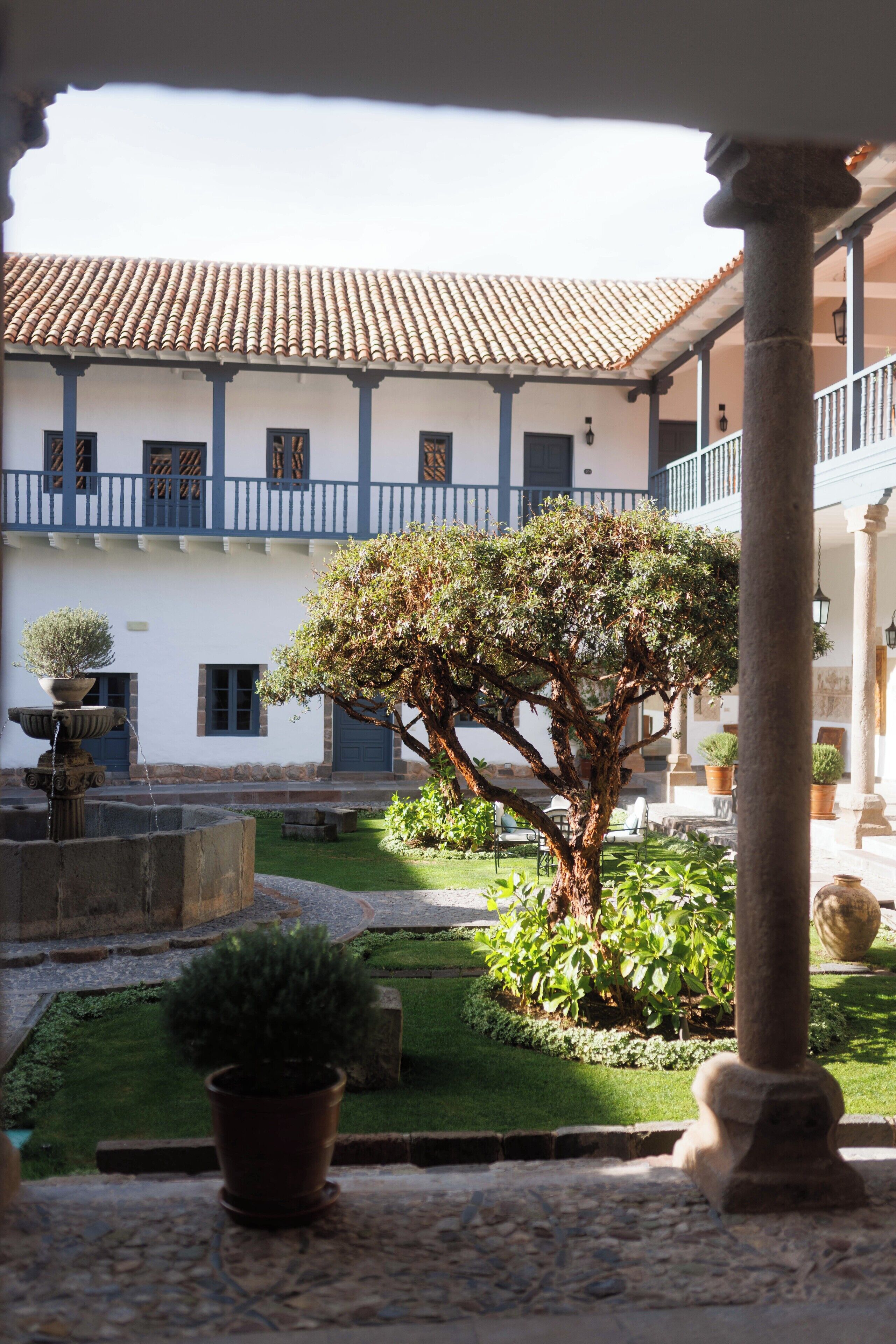 A courtyard with a large tree, a fountain, and a building with a tiled roof.